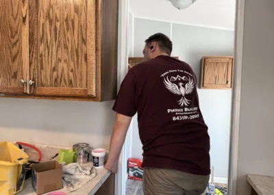 A worker in a maroon Phoenix Builders shirt performing maintenance on a doorframe next to kitchen cabinets