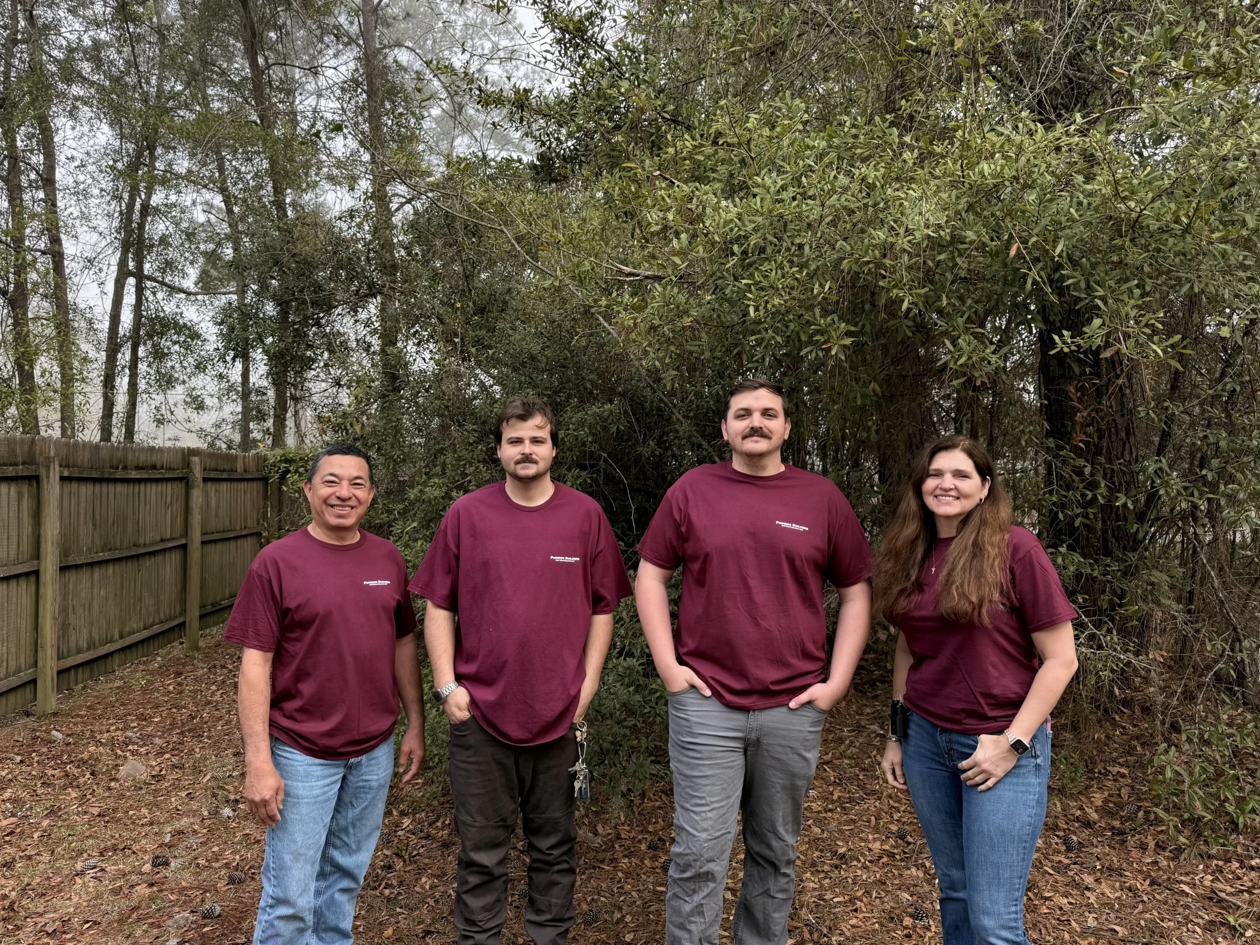 Four members of the Phoenix Builders team standing together in front of a wooded area and a wooden fence